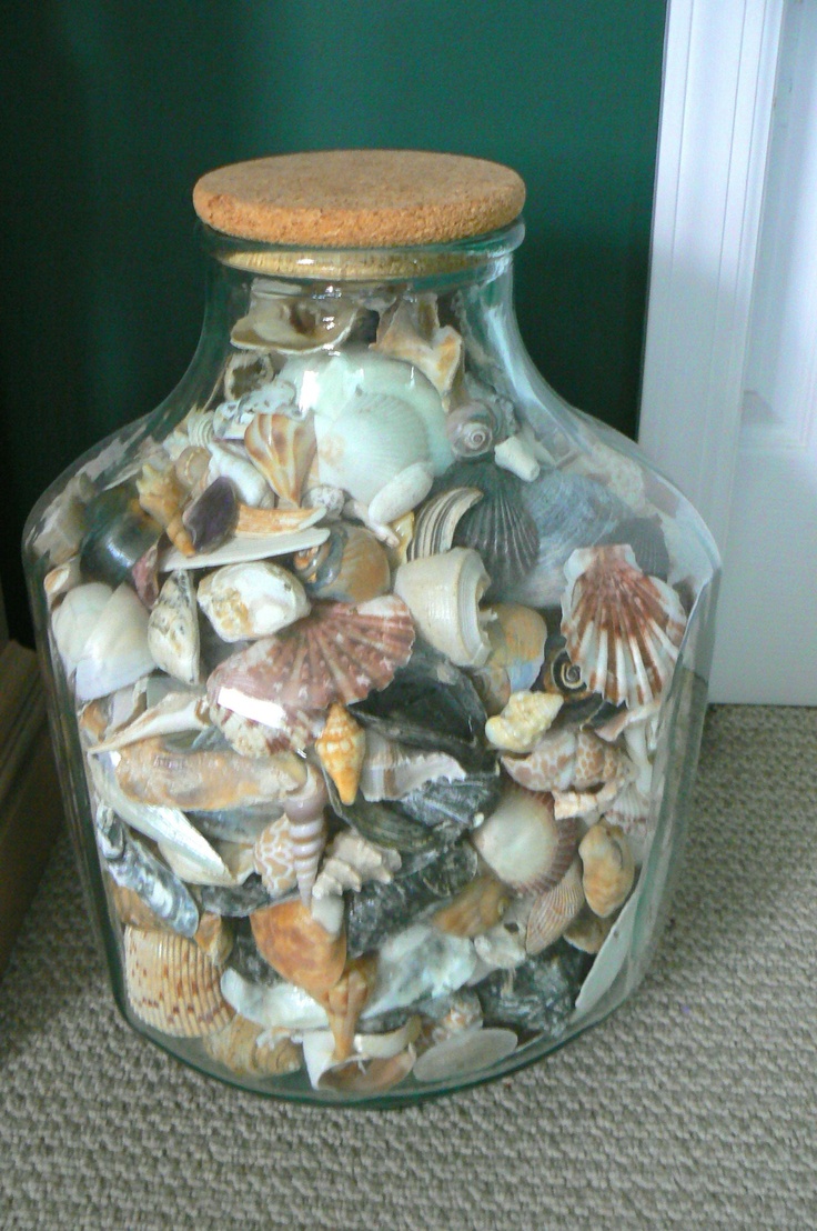 a glass jar filled with sea shells sitting on the floor next to a door way