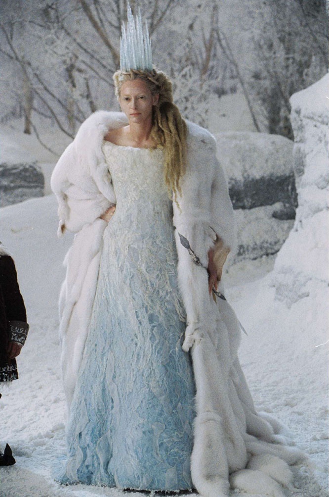 two people dressed in costumes standing next to each other on snow covered ground with trees behind them