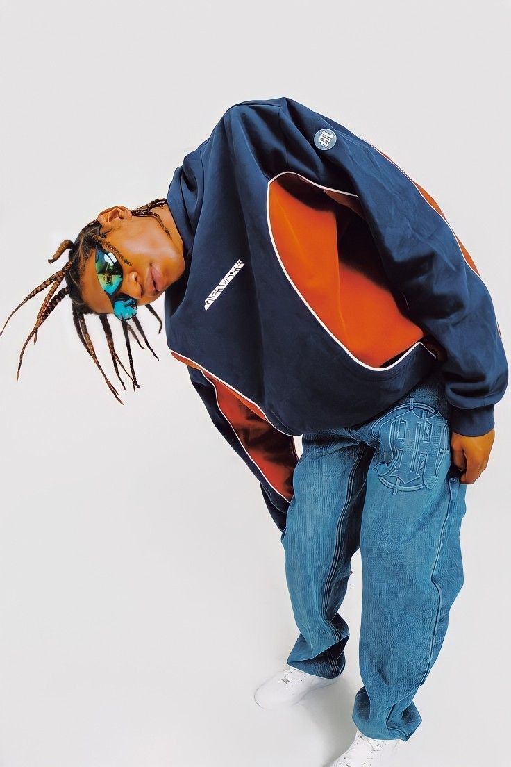 a young man with dreadlocks standing in front of a white background wearing an orange and blue jacket