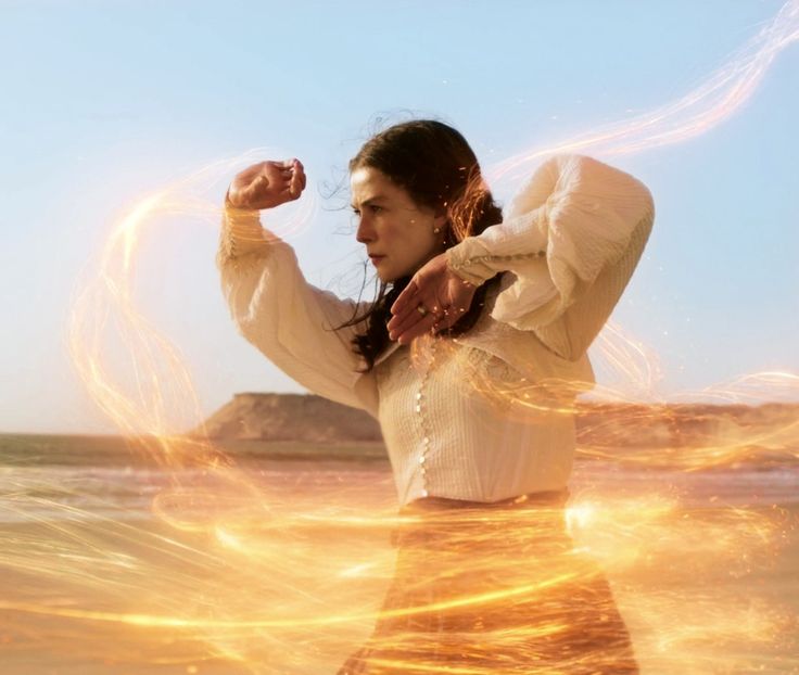 a woman standing on top of a beach next to the ocean with her arms in the air