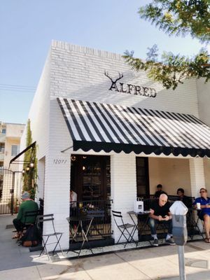 people are sitting at tables in front of a building with black and white awnings