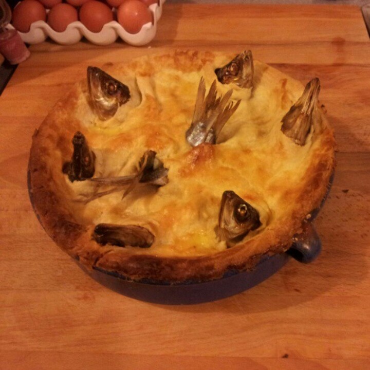 a close up of a pie on a wooden table with eggs in the back ground