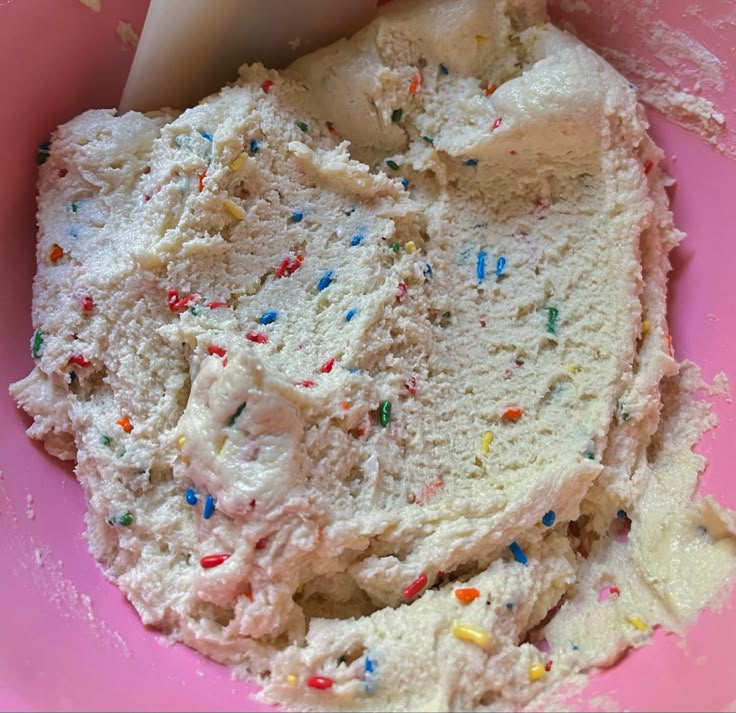 a pink bowl filled with white frosting and sprinkles