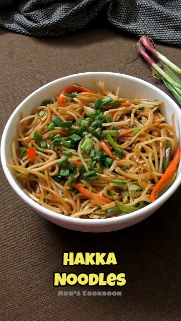 a white bowl filled with noodles and veggies on top of a brown table