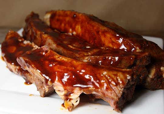 two pieces of meat sitting on top of a white plate covered in bbq sauce