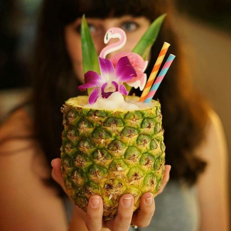 a woman holding up a pineapple with candles in it and a flamingo decoration on top