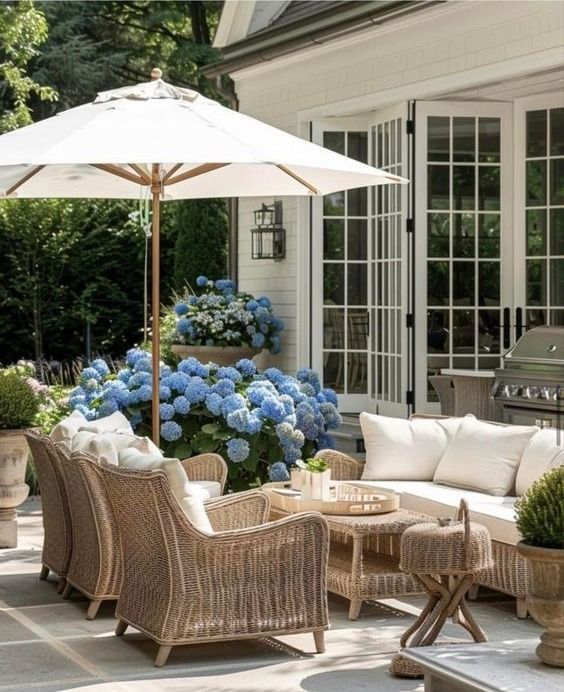 an outdoor living area with chairs, tables and umbrellas on the patio near blue hydrangeas