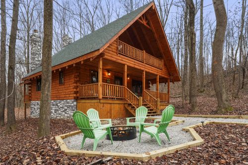 a log cabin in the woods with green chairs and a fire pit surrounded by leaves