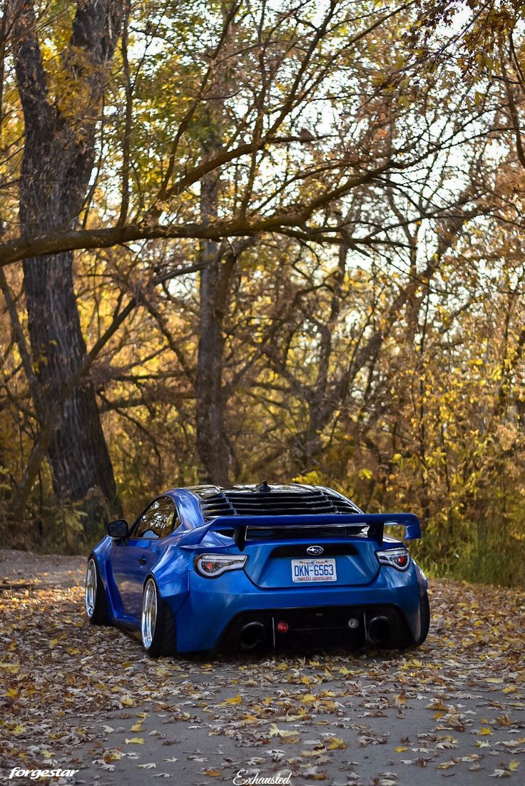 a blue sports car parked on the side of a road in front of some trees