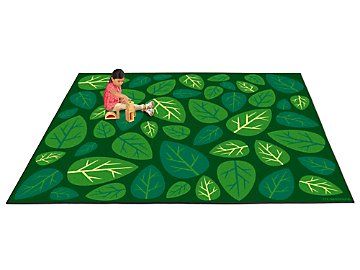 a person sitting on top of a green rug with leaves around it and a dog in the middle