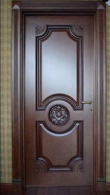 a wooden door with an ornate design on the top and bottom panel, in front of a green wall