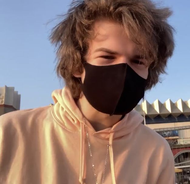 a young man wearing a black face mask in front of an empty stadium stands outside