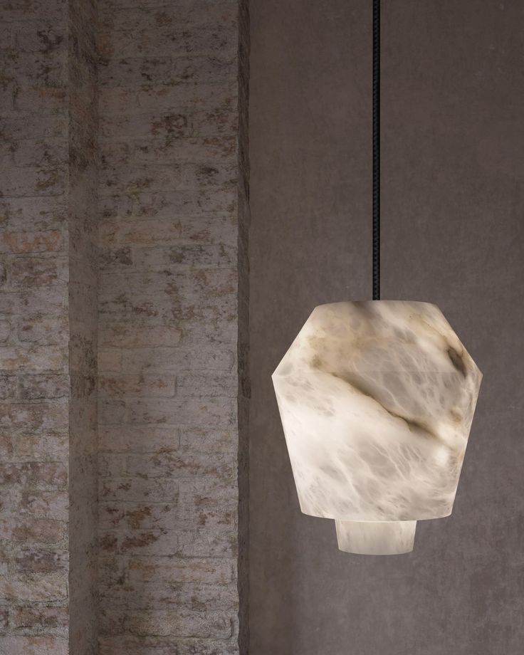 a white marble lamp hanging from a black cord in a room with concrete walls and flooring