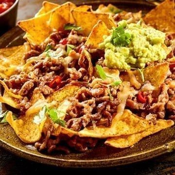 a plate full of nachos with guacamole and salsa on the side