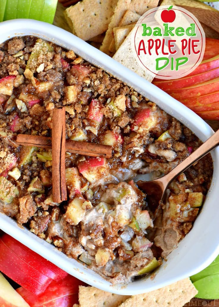 baked apple pie dip in a white casserole dish surrounded by apples and cinnamon sticks