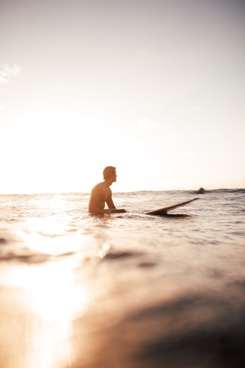 a man sitting on a surfboard in the middle of the ocean at sun set