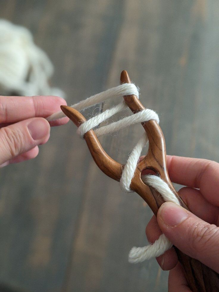 two hands are holding an object made out of wood and white yarn on a wooden table