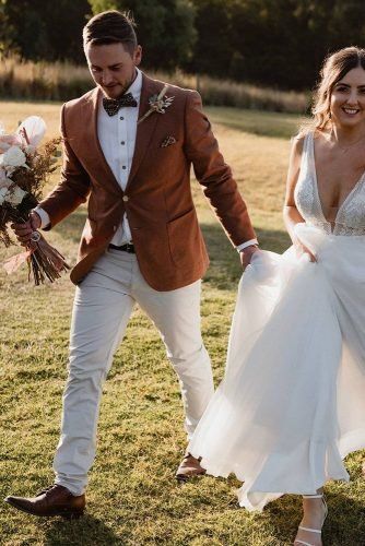 a bride and groom are walking through the grass holding hands with each other in their wedding attire