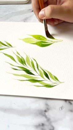 a person is painting leaves with watercolors on paper