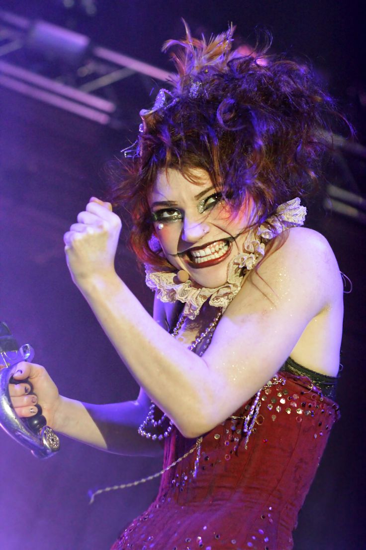 a woman in a red dress is holding a microphone and smiling at the camera while standing on stage