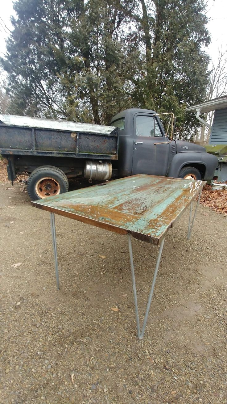 an old rusty table sitting in the middle of a dirt field next to a truck