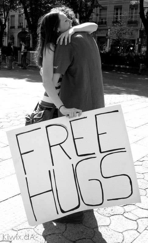 two people standing next to each other holding a free hugs sign