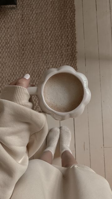 a woman is holding a coffee cup in her right hand while sitting on the floor