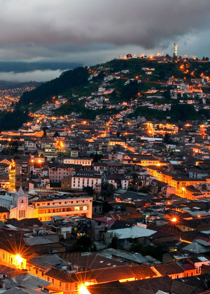 an aerial view of a city at night with lights on the buildings and mountains in the background