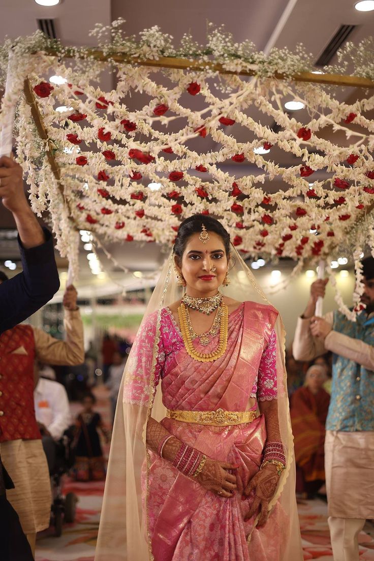 a woman in a pink sari is walking down the aisle with flowers hanging from the ceiling