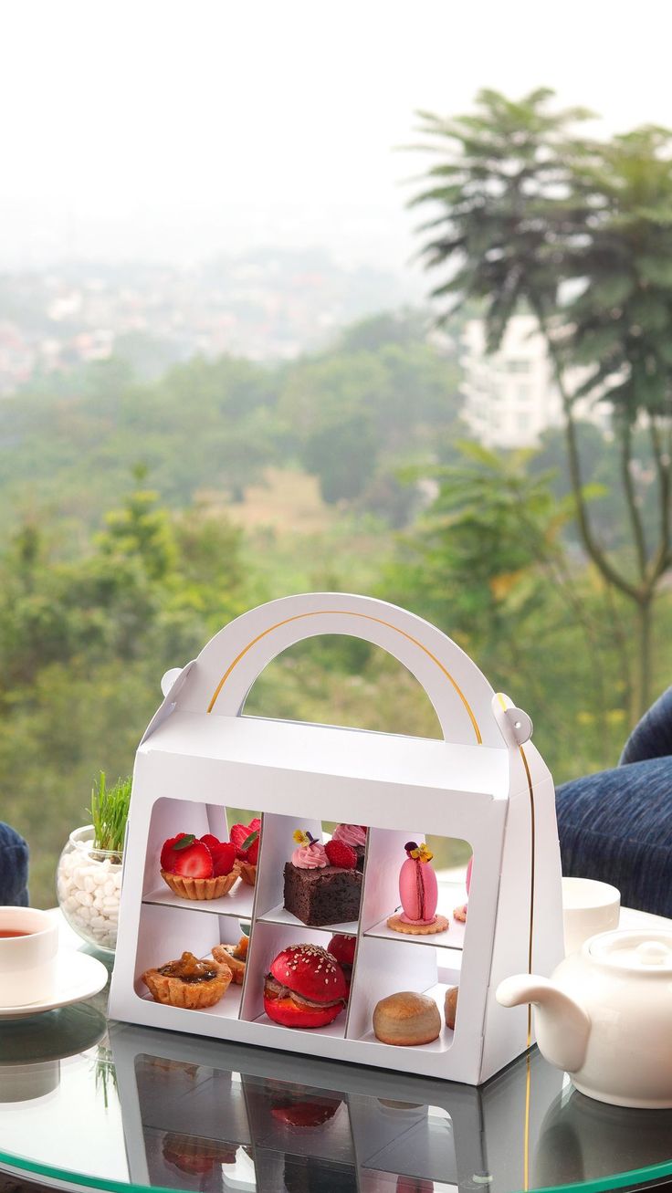 a tea set on a glass table in front of a window with trees and mountains behind it