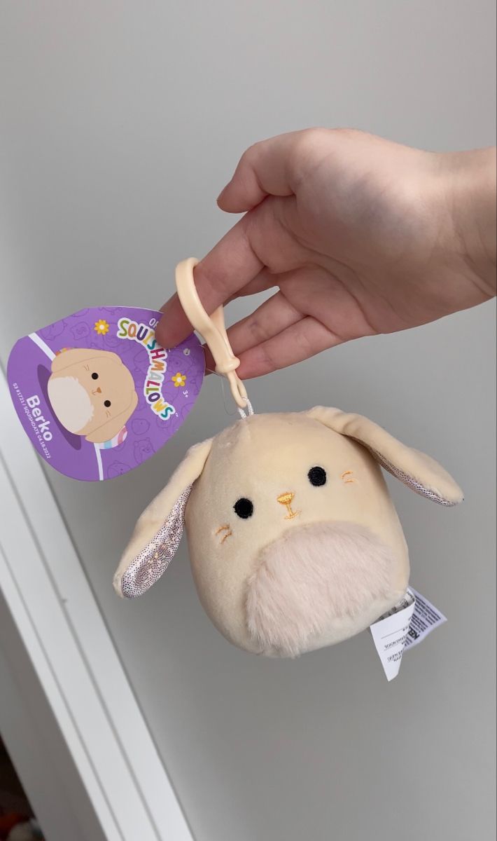 a hand holding a stuffed animal with a tag on it's ear and another toy in the background