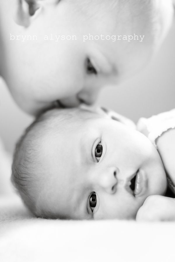 a woman is kissing a baby's face while laying on the bed in black and white