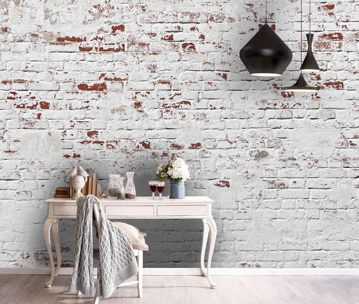 an old brick wall is painted white and has two lamps hanging from it, along with a small table