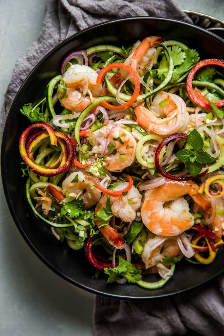 a black bowl filled with shrimp and veggies on top of a gray table