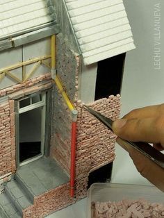 a hand holding a pair of scissors over a model house