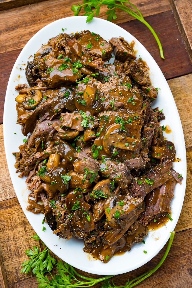 a white plate topped with meat and mushrooms on top of a wooden table next to parsley