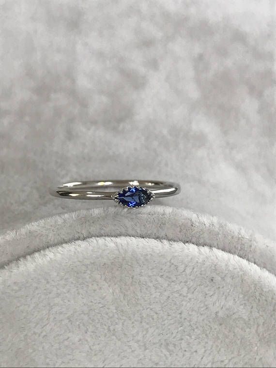 a white gold ring with a blue sapphire stone on the side, sitting on a gray velvet surface