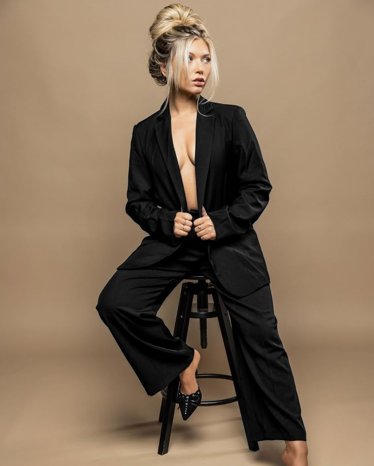 a woman sitting on top of a stool wearing black pants and a blazer jacket