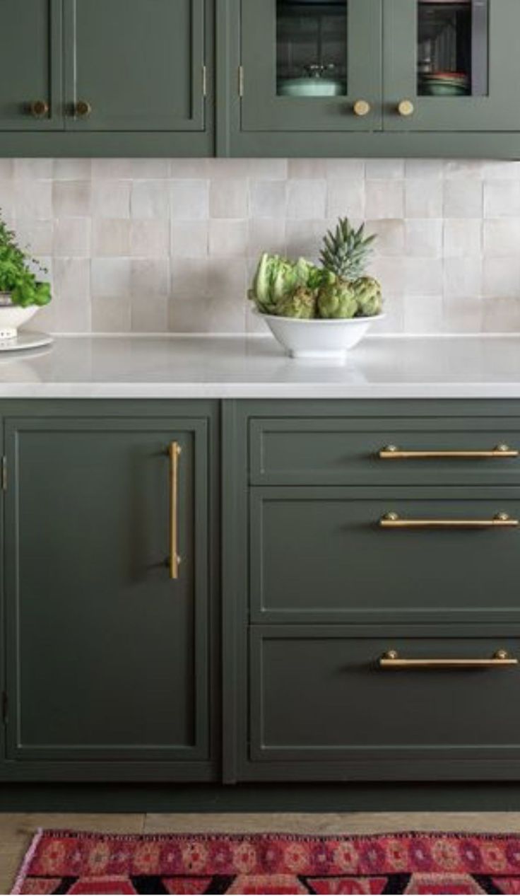 a kitchen with green cabinets and white counter tops, gold pulls on the handles in front of an area rug