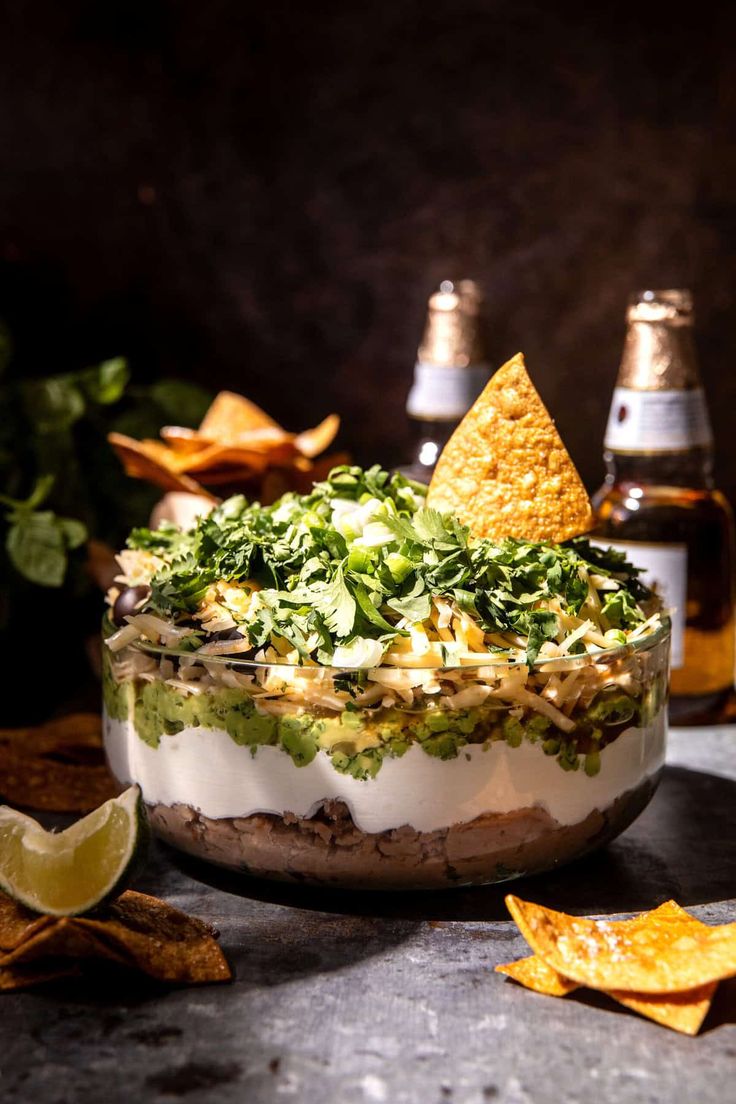 a bowl filled with food next to two bottles of beer and tortilla chips