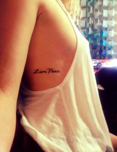 a woman wearing a white tank top has a tattoo on her left shoulder that says love free