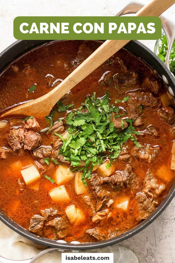 a pot filled with beef and potatoes next to a wooden spoon on top of a table