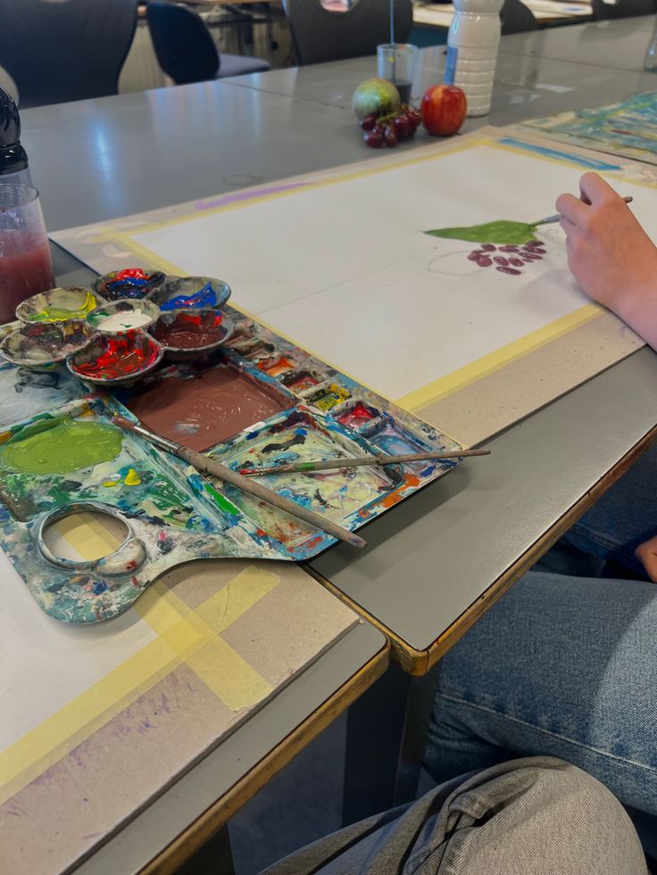 a person is sitting at a table with some paint and paper on top of it