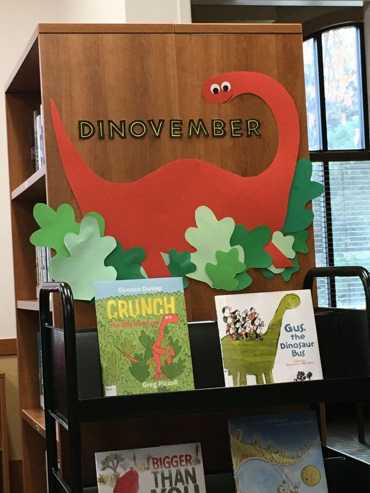 there is a book shelf with books on it and a dinosaur sign in the background