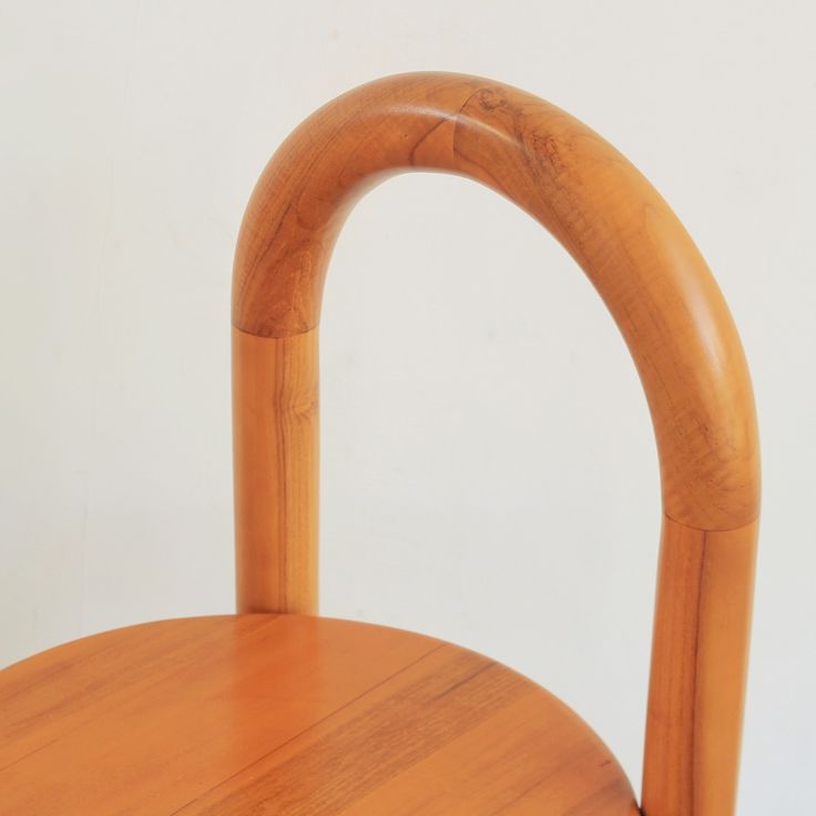 a close up of a wooden chair with a bent back and curved seat, against a white wall