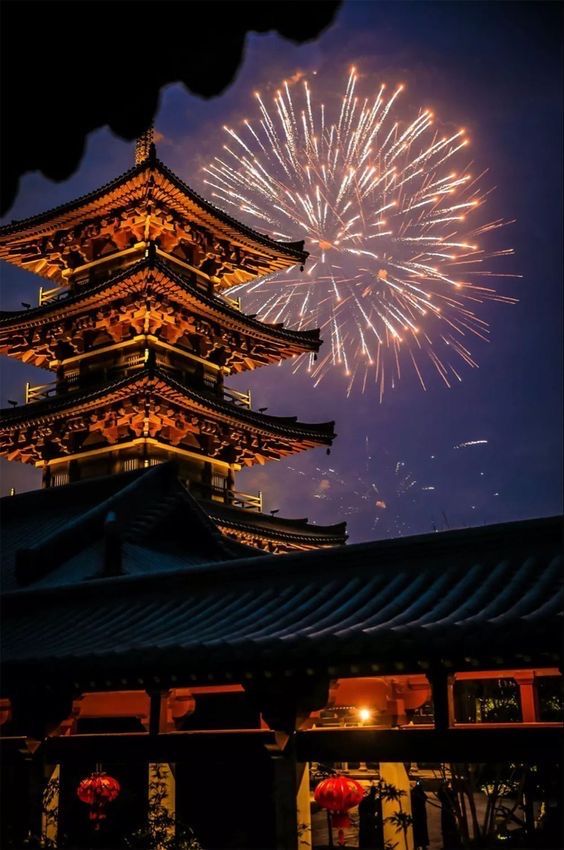 fireworks light up the sky above a tall building with a pagoda on it's roof