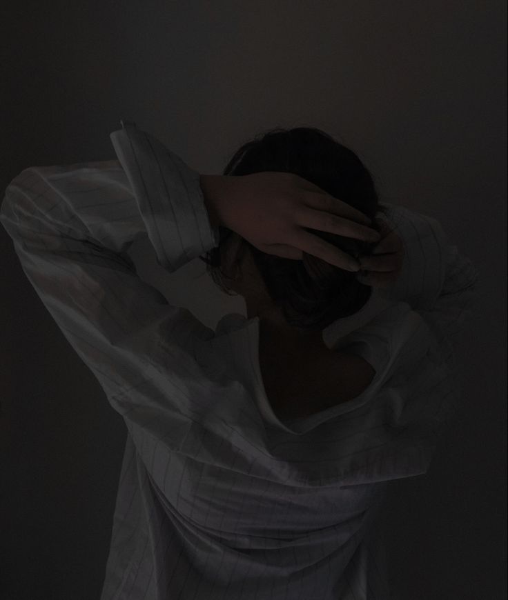 a woman is covering her head with her hands in the dark while standing against a wall