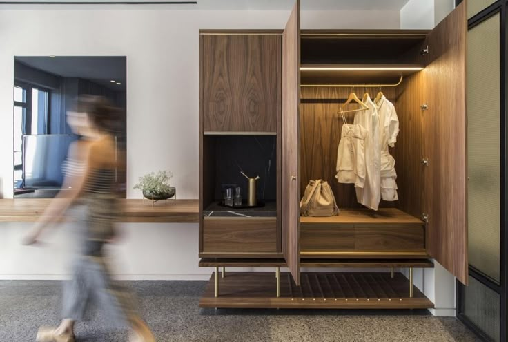 a blurry image of a person walking past a wooden cabinet with clothes on it