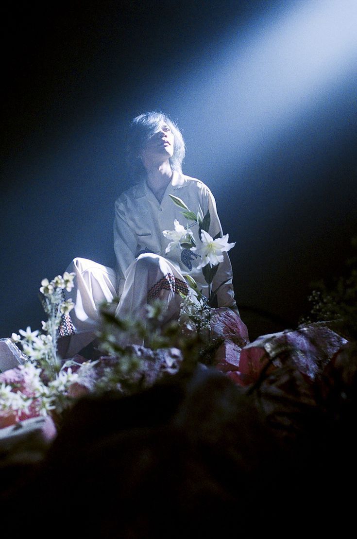 a man sitting on the ground with flowers in front of him and light coming from behind him