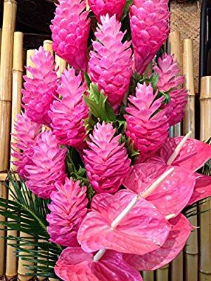 pink flowers are in a wicker basket next to bamboo sticks and palm fronds